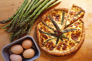 Overhead shot of asparagus quiche, a French vegetarian dish, with eggs and raw fresh asparagus