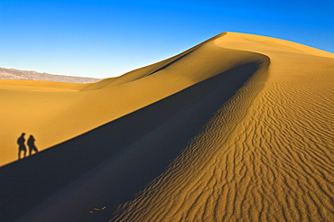 Shadows of two people walking up the dunes of the Mesquite Flats sand dunes, Grapevine Mountains of the Amargosa range behind, Stovepipe Wells, Death Valley National Park, California, United States of America, North America