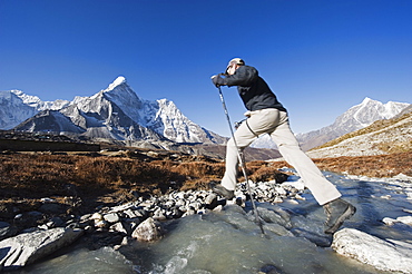 Trekker crossing a mountain stream, Ama Dablam, 6812m, behind, Solu Khumbu Everest Region, Sagarmatha National Park, Himalayas, Nepal, Asia