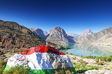 Iskanderkul Lake with a large rock painted in the colours of the Tajikistan flag in the foreground, Fan Mountains, Tajikistan, Central Asia, Asia