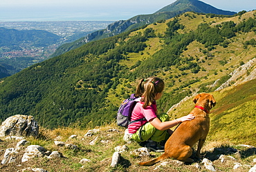 Girl and dog, looking at view of Camaiore and Tyrrhenian Sea from Apuan Alps (Alpi Apuane), Lucca Province, Tuscany, Italy, Europe