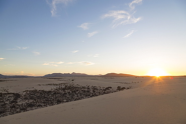 The sun setting over the dramatic Dunas de Corralejo on the volcanic island of Fuerteventura with mountains beyond, Fuerteventura, Canary Islands, Spain, Europe