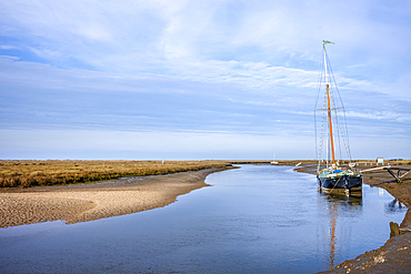 Moored yacht on the banks of the River Glaven, with marshes beyond, at Blakeney in North Norfolk