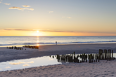 Woman standing next to wooden groynes on Rantum beach at sunset, Sylt, Schleswig Holstein, Germany, Europe