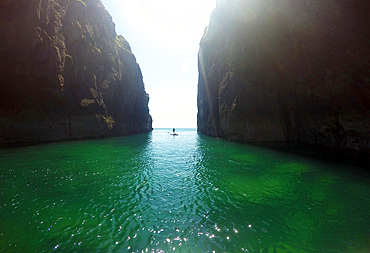 Paddle boarder exploring cliffs and rock architecture on the Pembrokeshire Coast, Wales, United Kingdom, Europe