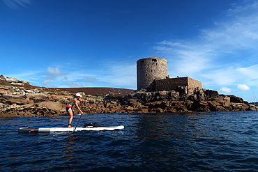 Paddle boarder under Cromwell's Castle, a castle built during the English Civil War on the west coast of Tresco, Isles of Scilly, England, United Kingdom, Europe