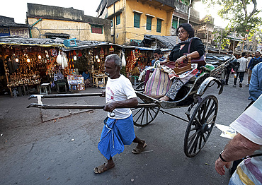 Old style running rickshaw wallah pulling woman and her shopping through Kolkata streets away from the Kali temple, Kolkata (Calcutta), West Bengal, India, Asia