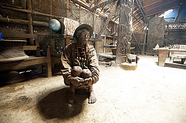 Naga man, Longsha Wangnao, head hunter, with tattooed face and Naga necklace, sitting in communal Naga tribal house, Longwa, Nagaland, India, Asia