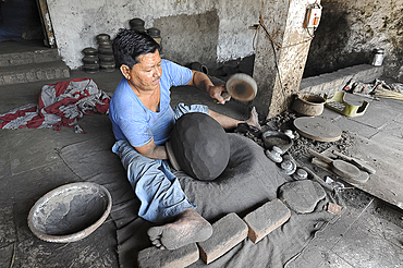 Man beating hand made charcoal dusted terracotta water jar into traditional shape with a wooden paddle, Chhote Udepur, Gujarat, India, Asia