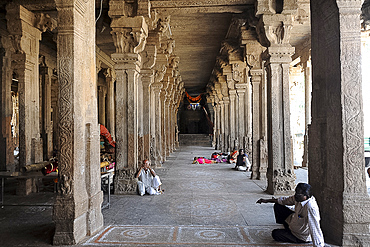 People resting in the stone pillared corridor inside the 11th century Brihadisvara Cholan temple, Thanjavur, Tamil Nadu, India, Asia