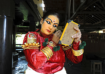 Performer carefully applying make-up with bamboo stick for a Kathakali dance performance of folk mythologies, Nilambur, Kerala, India, Asia