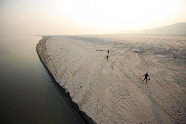 Three men at sunrise releasing ropes from a mooring in the fine sand of a seasonal sandspit, Brahmaputra River, Assam, India, Asia