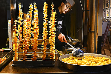 Man cooking fried spiralled potato on long sticks for sale in Muslim quarter night market, Xian, Shaanxi, China, Asia