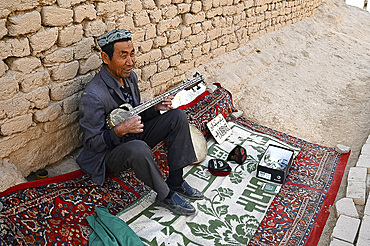 Uyghur man playing a Rawap, traditional Uyghur lute, in Gaochang, ruined Silk Road city, Xinjiang, China, Asia