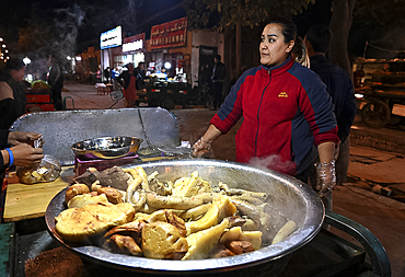 Woman selling cooked meats from rickshaw stall in Turfan night market, Turfan, Xinjiang, China, Asia