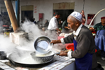 Uyghur Muslim man cooking noodles at noodle stall in Kashgar Sunday Market, Kashgar, Xinjiang, China, Asia