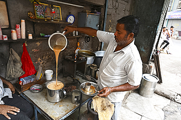 Busy chaiwallah pouring tea at a chai stall in the palls (alleyways) of old Ahmedabad, Gujarat, India, Asia