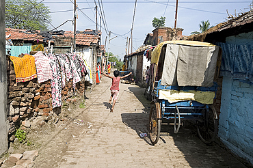 Child running down narrow street in Hooghly past cycle rickshaw and washing hanging over brick walls, West Bengal, India, Asia