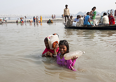 Mother and daughter wading across the River Ganges holding bottles of Holy River Ganges water, Sonepur, Bihar, India, Asia