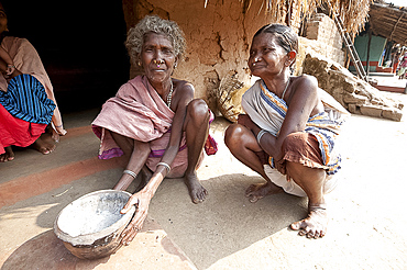 Two Desia Kondh tribal women squatting outside their village house holding welcome bowl of ash, Bissam Cuttack, Orissa, India, Asia