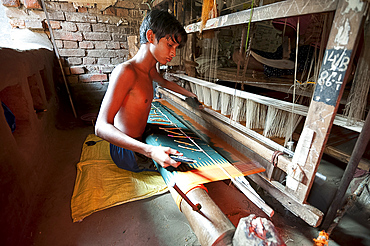 Young boy at domestic loom weaving patterned silk sari using several spools of silk, Vaidyanathpur weaving village, Orissa, India, Asia