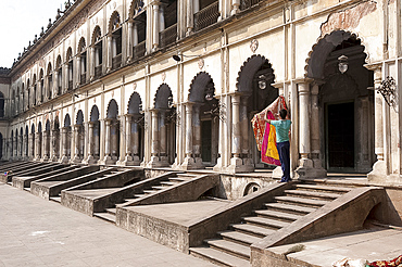 Man hanging out washed Quran cover cloths outside arched madrasa rooms in the Hugli Imambara, Hugli, West Bengal, India, Asia