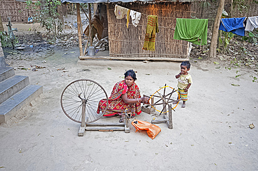 Woman spinning silk on home made spinning wheel made from wood and bicycle wheel, in rural village, West Bengal, India, Asia