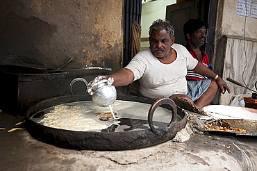 Jalebi wallah dripping sweet rice flour paste into hot fat to make jalebi in street snack stall, Kolkata, West Bengal, India, Asia