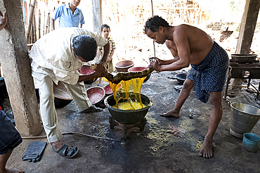 Two men squeezing yellow dye out of cotton fabric over a metal bowl heated over gas flame, Naupatana weaving village, rural Orissa, India, Asia