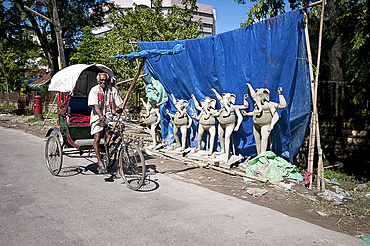 Cycle rickshaw passing row of Ganesh deities made from mud from the Brahmaputra River in preparation for Durga puja celebrations, Guwahati, Assam, India, Asia