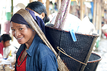 Smiling Naga woman wearing traditional woven cane head basket, shopping in Tizit village weekly local market, Nagaland, India, Asia