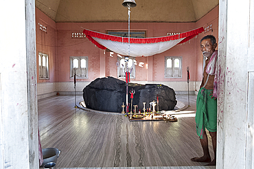 Pundit cum caretaker of holy rock from the Brahmaputra, painted black, in the village Shiva temple on the Brahmaputra riverbank, Assam, India, Asia