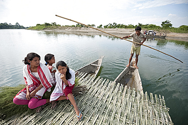 Young girls wearing traditional Assamese gamosa scarves, on simple ferry being poled across the Brahmaputra river, Assam, India, Asia