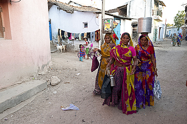 Three women in colourful saris, returning from the well with oil can and pots full of water in main village street, Dasada, Gujarat, India, Asia