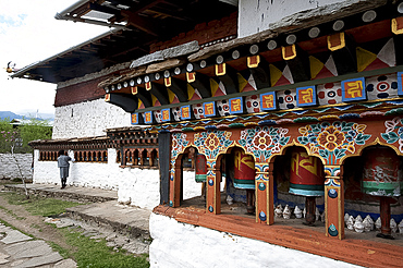 Buddhist man spinning temple prayer wheels outside Dumtse Lakhang Buddhist temple as he perambulates the temple before entering, Bhutan, Asia