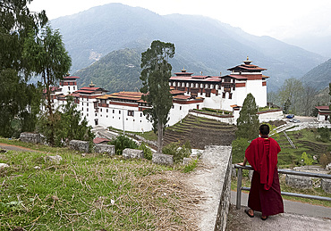 Buddhist monk looking back at Trongsa Dzong, Bhutan's largest monastery fortress established in 1543 above Mangde river gorge, Bhutan, Asia