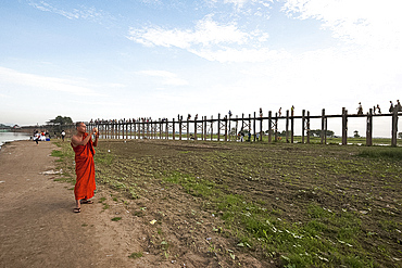 Orange robed monk photographing people crossing U Bein's Bridge, supported by 984 teak posts over Thaumthaman Lake, Mandalay, Myanmar (Burma), Asia