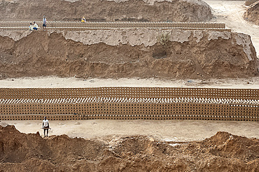 Brick workers amongst hand made bricks laid out on the ground to dry before baking, northeast of Jaipur, Rajasthan, India, Asia