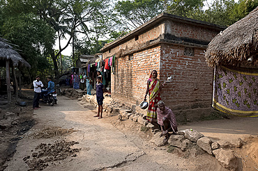 Villagers in typical rural village afternoon scene in the street outside a modern laterite brick built village house, Odisha, India, Asia