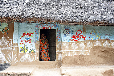 Woman at the door of traditional mud walled Odisha village house decorated with traditional Odishan patterns, Dandasahi, Odisha, India, Asia