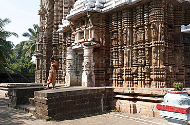 Hindu priest in saffron robes outside ornately carved 13th century Madhava temple dedicated to Lord Vishnu, Madhava, Odisha, India, Asia