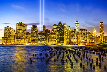 Lower Manhattan skyscrapers including One World Trade Center from across the East River at night, with light beams from the Tribute in Light 9/11 Memorial, New York City, New York, United States of America, North America