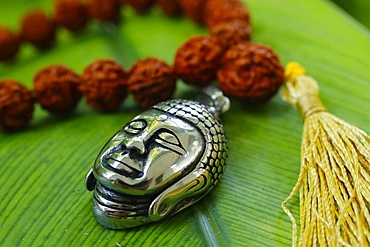 Silver Buddha medallion and prayer beads (mala) on a green leaf, Kep, Cambodia, Indochina, Southeast Asia, Asia