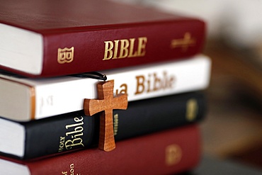 Four different Bibles and a Christian cross on a table, France, Europe