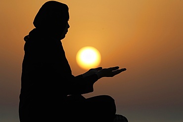 Silhouette of a Muslim woman in abaya praying with her hands at sunset, United Arab Emirates, Middle East