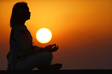 Woman practising yoga pose and meditation at sunset as concept for silence and relaxation, United Arab Emirates, Middle East