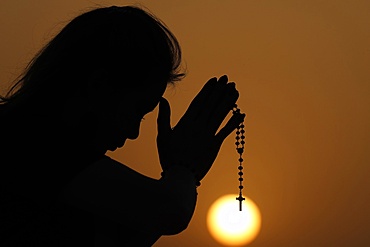 Silhouette of faithful woman praying with rosary beads at sunset as concept for religion, faith, prayer and spirituality, Dubai, United Arab Emirates, Middle East