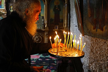 Monk tidying candles in Orhei Vecchi Monastery, Orhei, Moldova, Europe