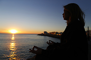 Woman practising yoga meditation by the sea at sunset as concept for silence and relaxation, Cadiz, Andalucia, Spain, Europe