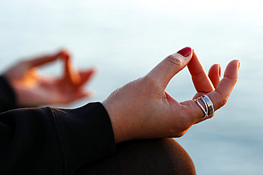 Woman practising yoga meditation by the sea at sunset as concept for silence and relaxation, close-up on hand, gyan mudra, Spain, Europe